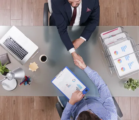 Insurance agent and trucking client shaking hands over a desk